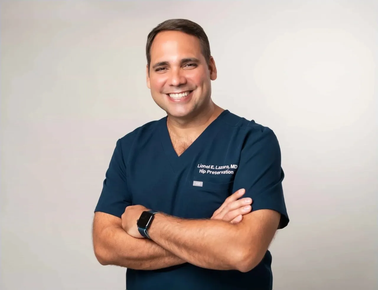 Dr. Lázaro con uniforme quirúrgico azul marino y brazos cruzados